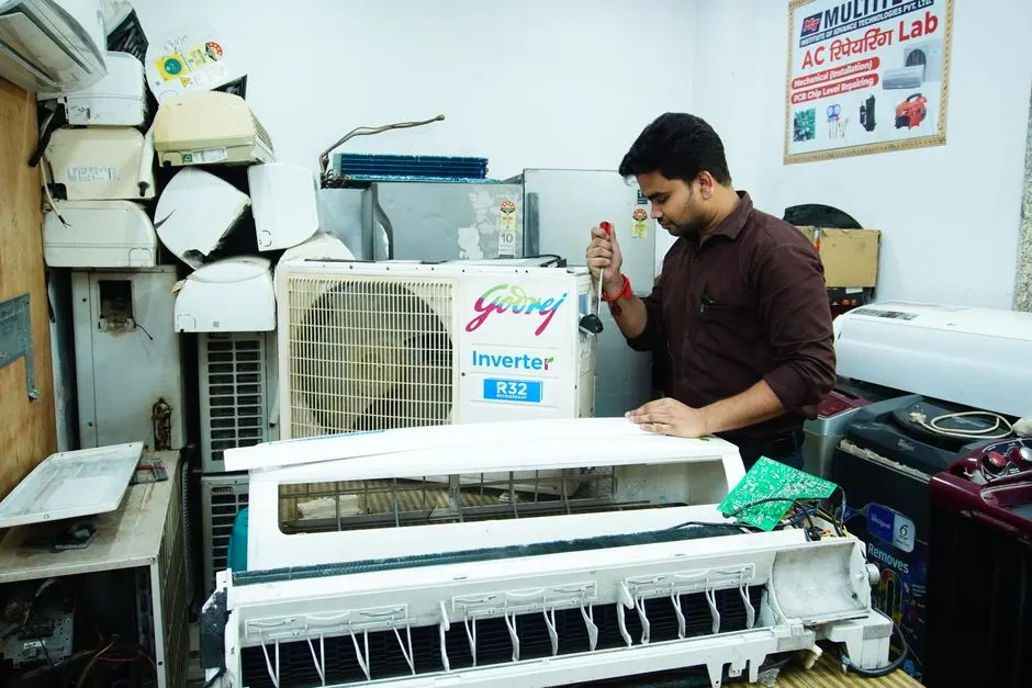 Technician repairing an air conditioner unit in New Delhi workshop.